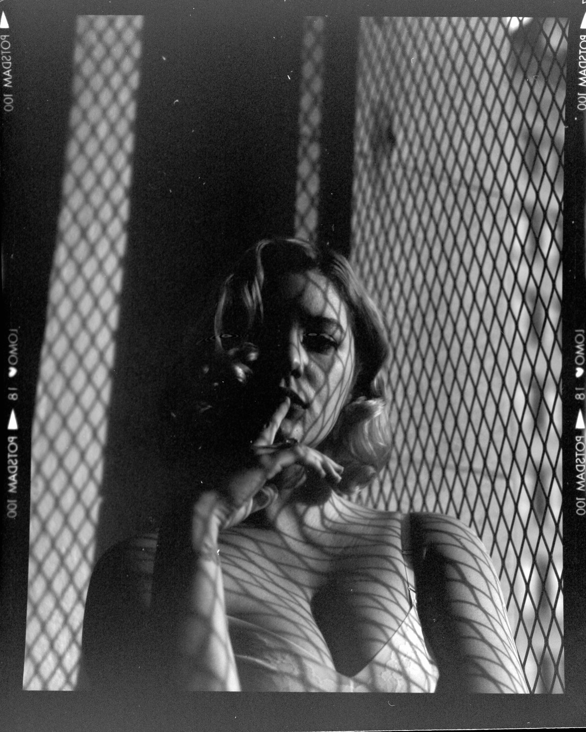 A woman with her finger to her lips is covered in shadows from a grid pattern.