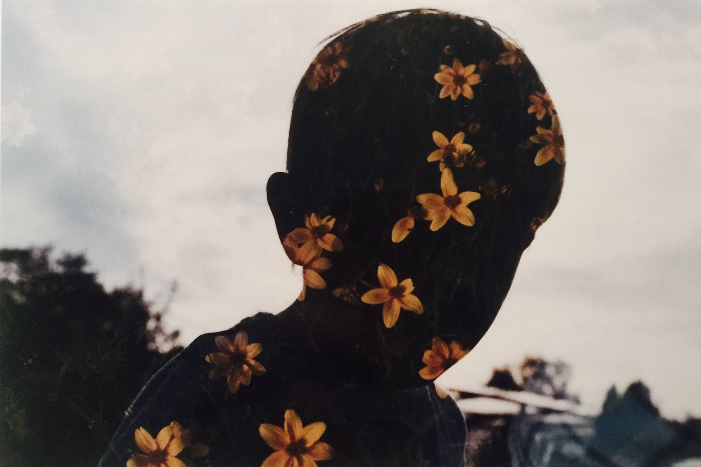 A double exposure shows the silhouette of a child filled with yellow flowers against a cloudy sky.