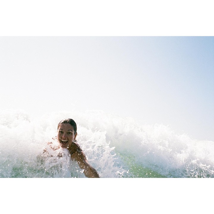 A woman with a joyful expression is surrounded by a breaking wave.