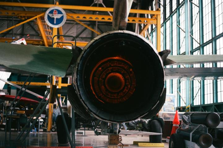 The rear of a jet engine with a glowing orange interior is visible in a hangar.