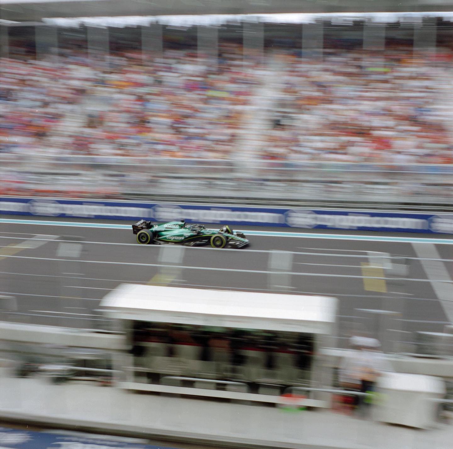 A green race car speeds along a track with blurred spectators in the background.