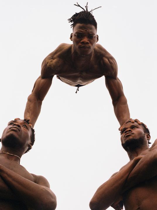 Three men form a human pyramid with one man balancing on the heads of the other two.