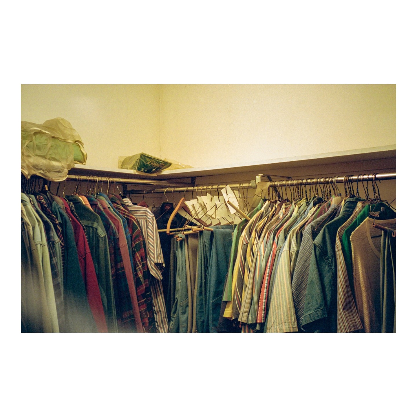 A closet is filled with various clothes hanging on a metal rod, with some items stored on a shelf above.