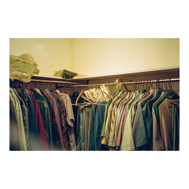 A closet is filled with various clothes hanging on a metal rod, with some items stored on a shelf above.