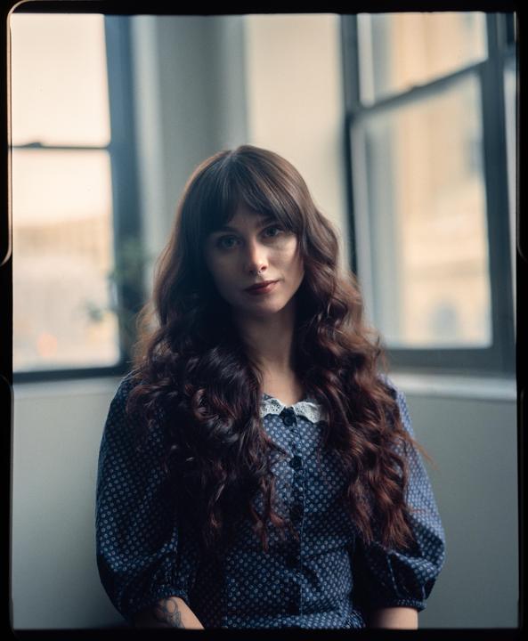 A woman with long, wavy hair and a polka dot dress looks directly at the viewer.