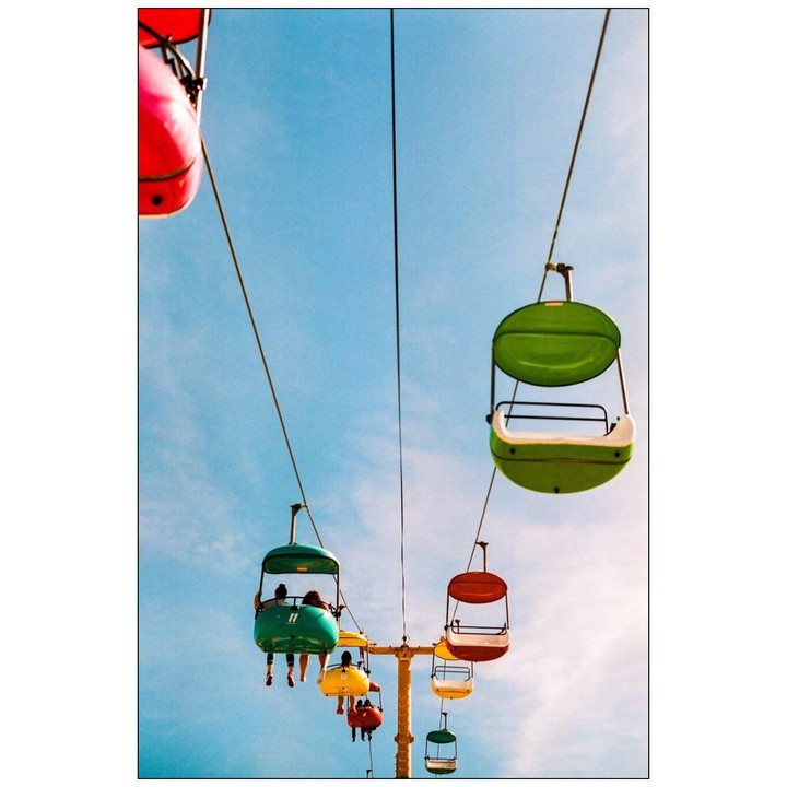 Colorful gondolas with people in them are suspended in the air against a bright blue sky.