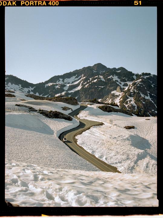 A winding road cuts through a snow-covered mountain landscape under a clear sky.