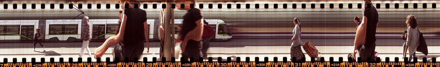 A slit-scan photograph shows people walking on a platform next to a moving tram.