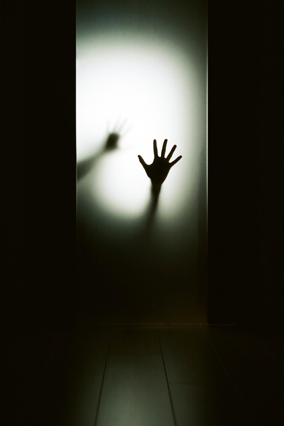 A shadowy hand presses against a frosted glass door, with another hand visible in the blurry background.