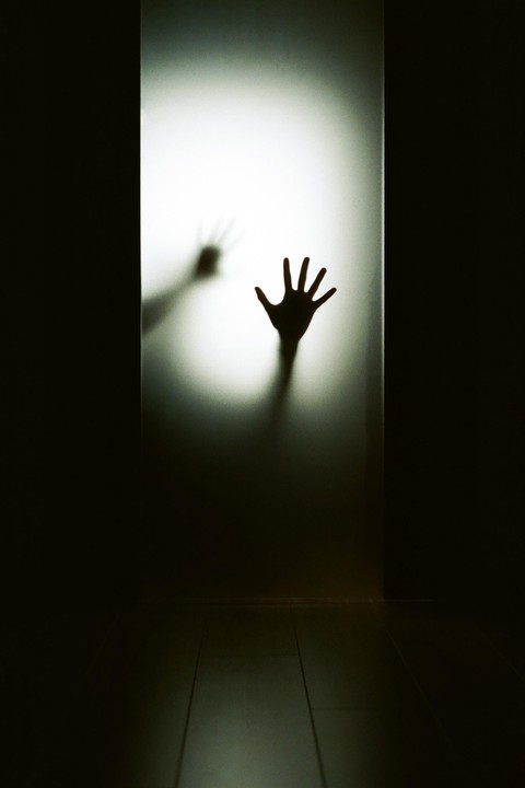 A shadowy hand presses against a frosted glass door, with another hand visible in the blurry background.