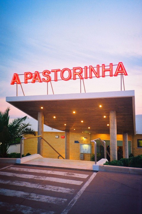 A red neon sign for "A Pastorinha" is visible above a building entrance with a crosswalk in the foreground.