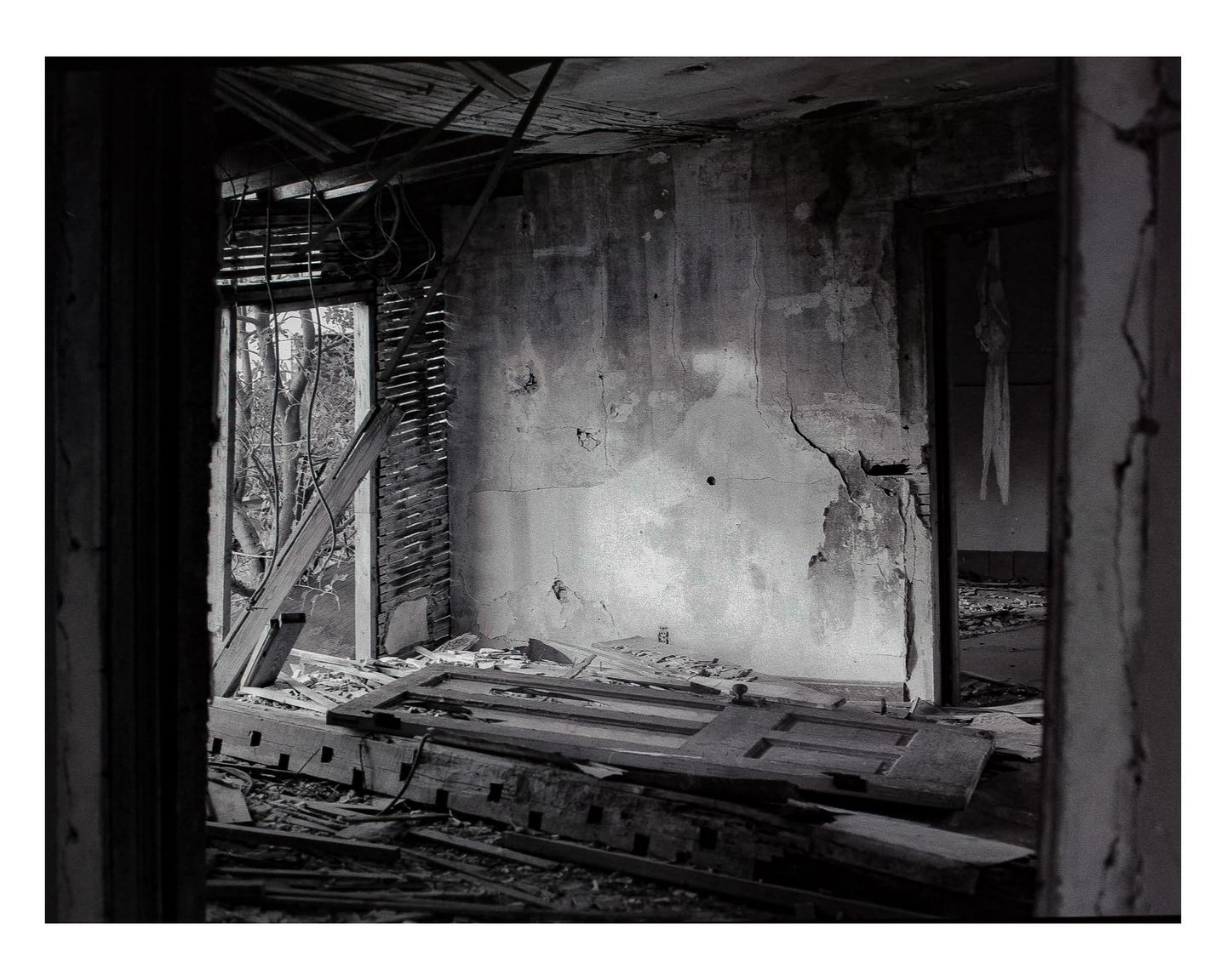 A derelict room with a collapsed ceiling and debris on the floor is illuminated by light from an open doorway.