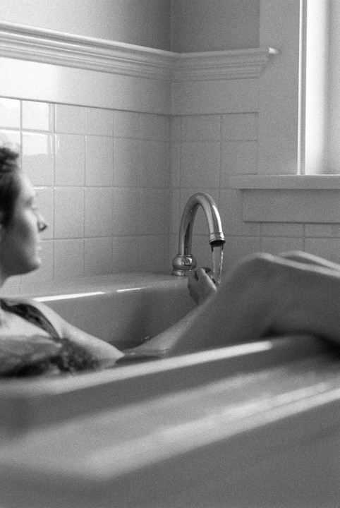 A woman is taking a bath, with water running from the faucet.