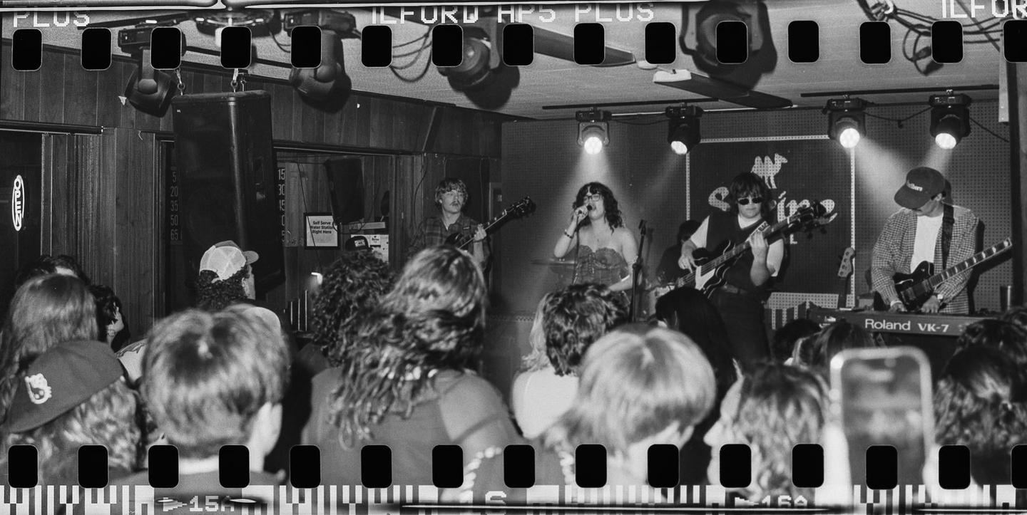 A band performs on stage in a dark venue with a crowd watching.