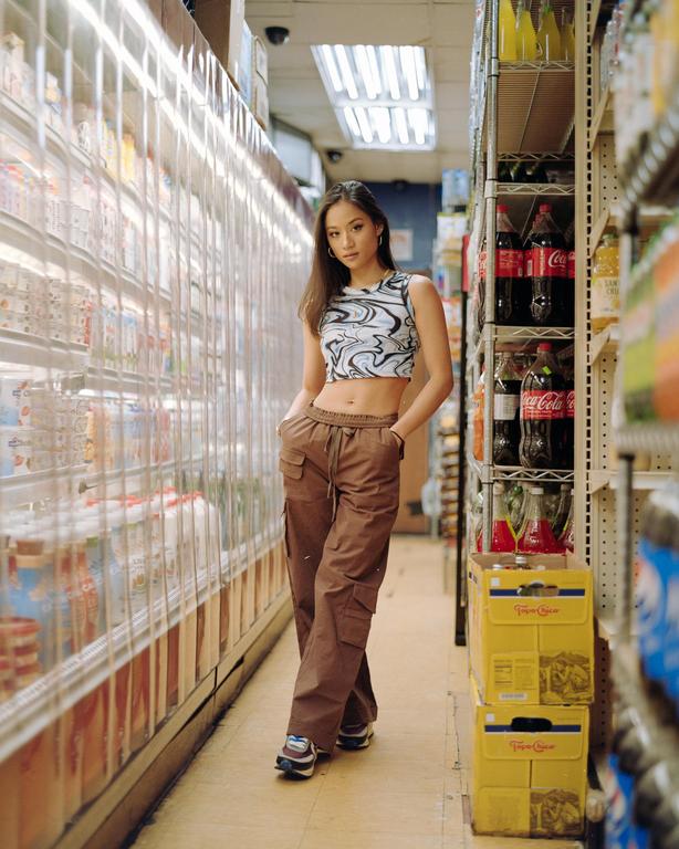 A woman stands in an aisle between refrigerated cases and shelves of drinks in a store.