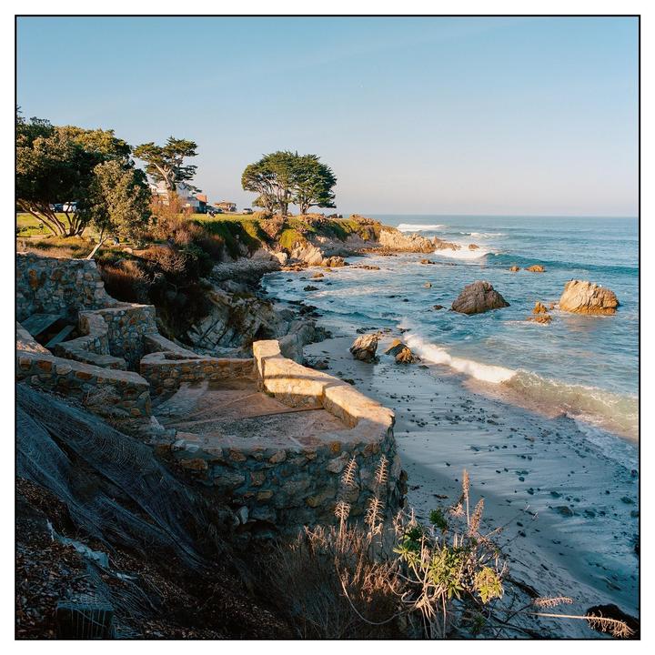 A stone wall and steps lead down to a sandy beach with waves crashing on the shore.