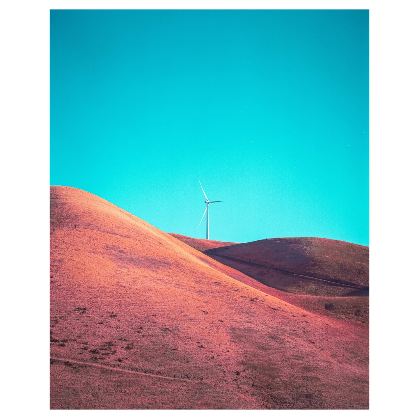 A wind turbine stands on a hill under a bright blue sky.