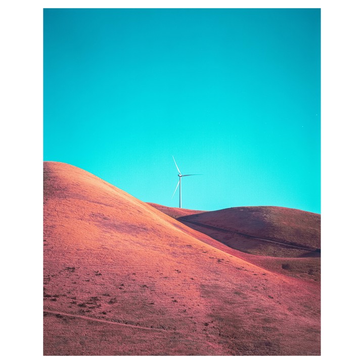 A wind turbine stands on a hill under a bright blue sky.