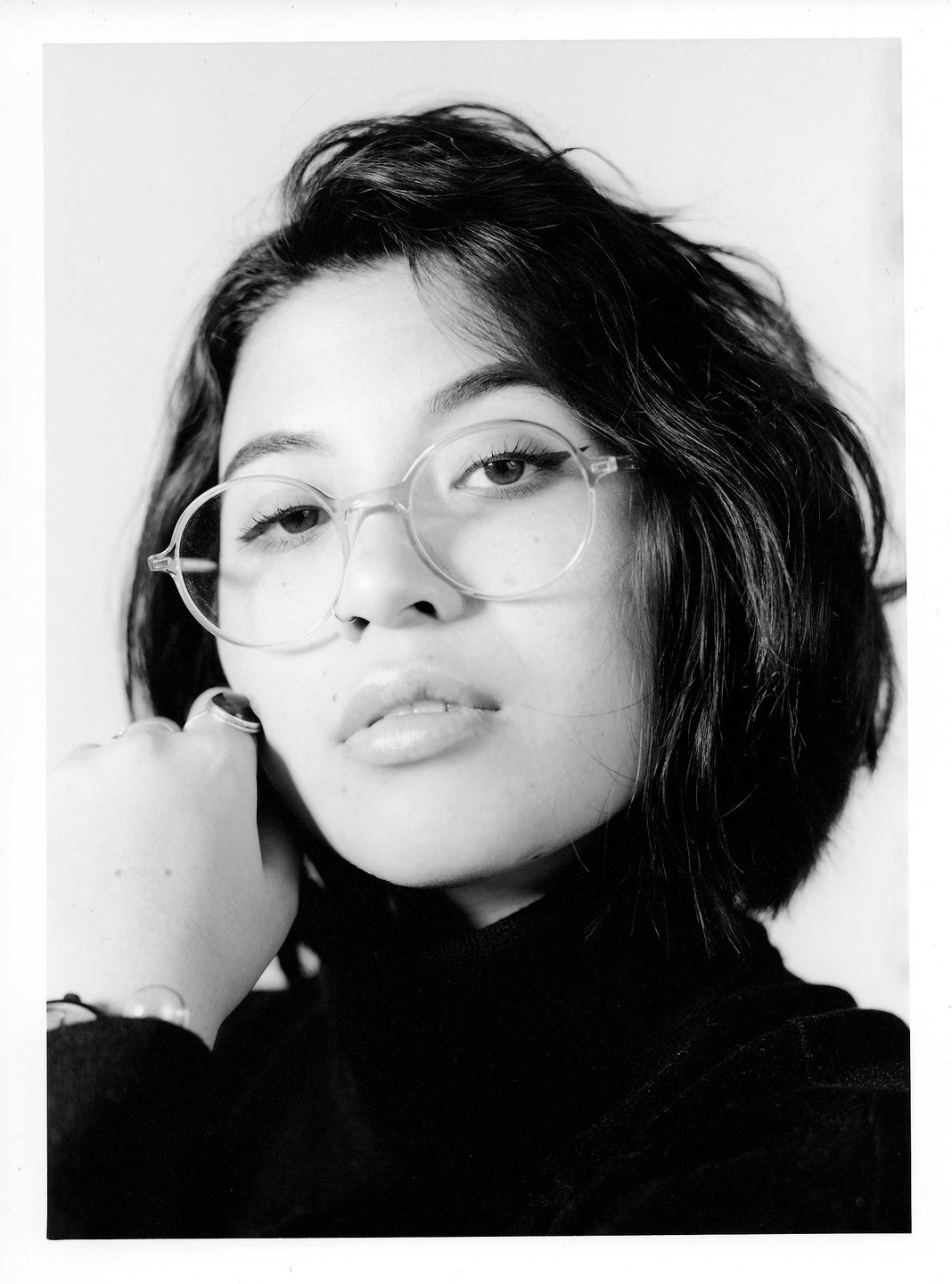 A woman with short hair and glasses looks directly at the viewer.