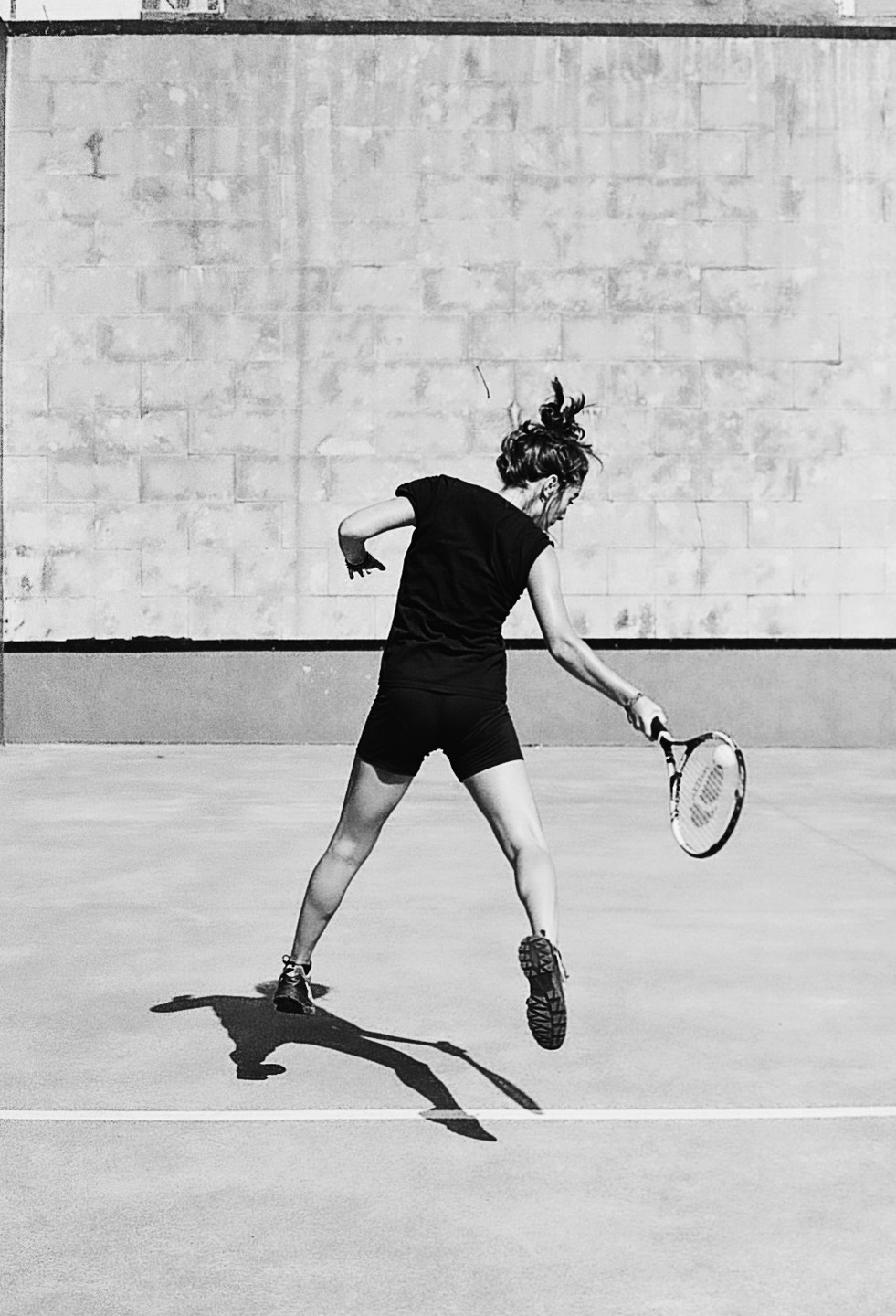 A woman plays frontenis on a court with a racket in her hand.
