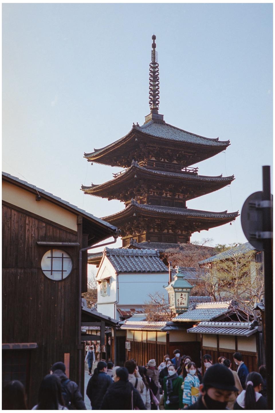 A five-story pagoda rises above a street lined with traditional Japanese buildings and people.