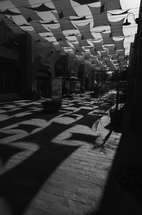 A street is covered by a canopy of fabric squares, casting strong shadows on the ground.