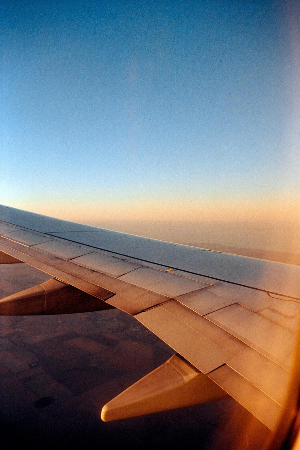 An airplane wing is visible against a clear sky and distant land during descent.