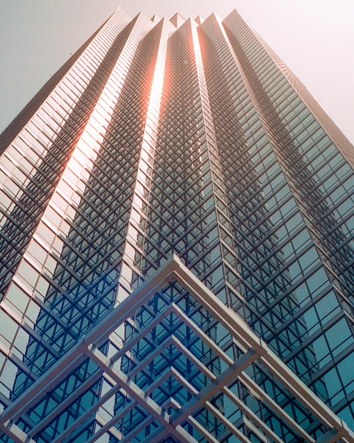 A low-angle view shows a tall glass building with a bright sun flare on its facade.