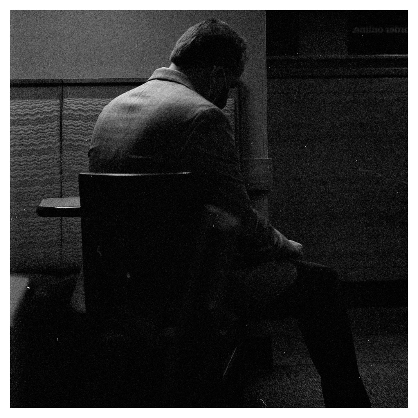 A man sits with his back to the viewer in a dimly lit room.