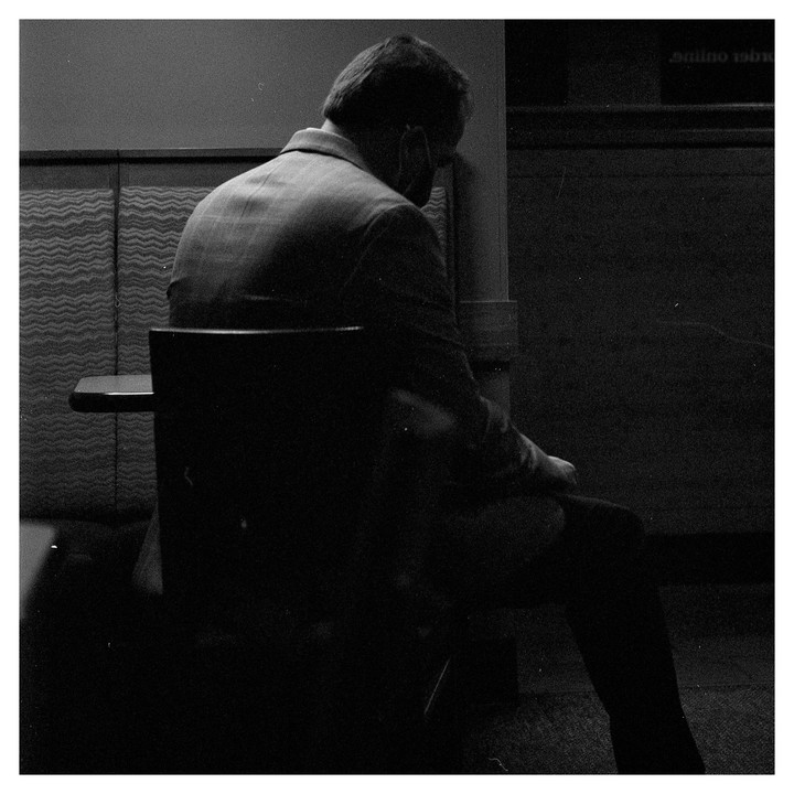 A man sits with his back to the viewer in a dimly lit room.