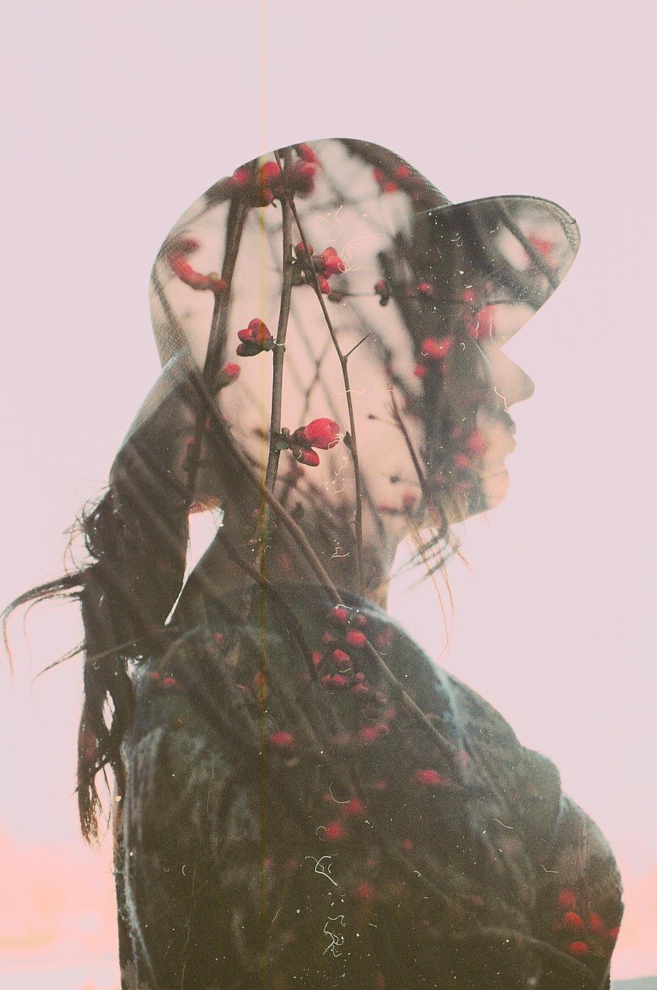 A double exposure shows the silhouette of a woman wearing a hat overlaid with branches of red blossoms.
