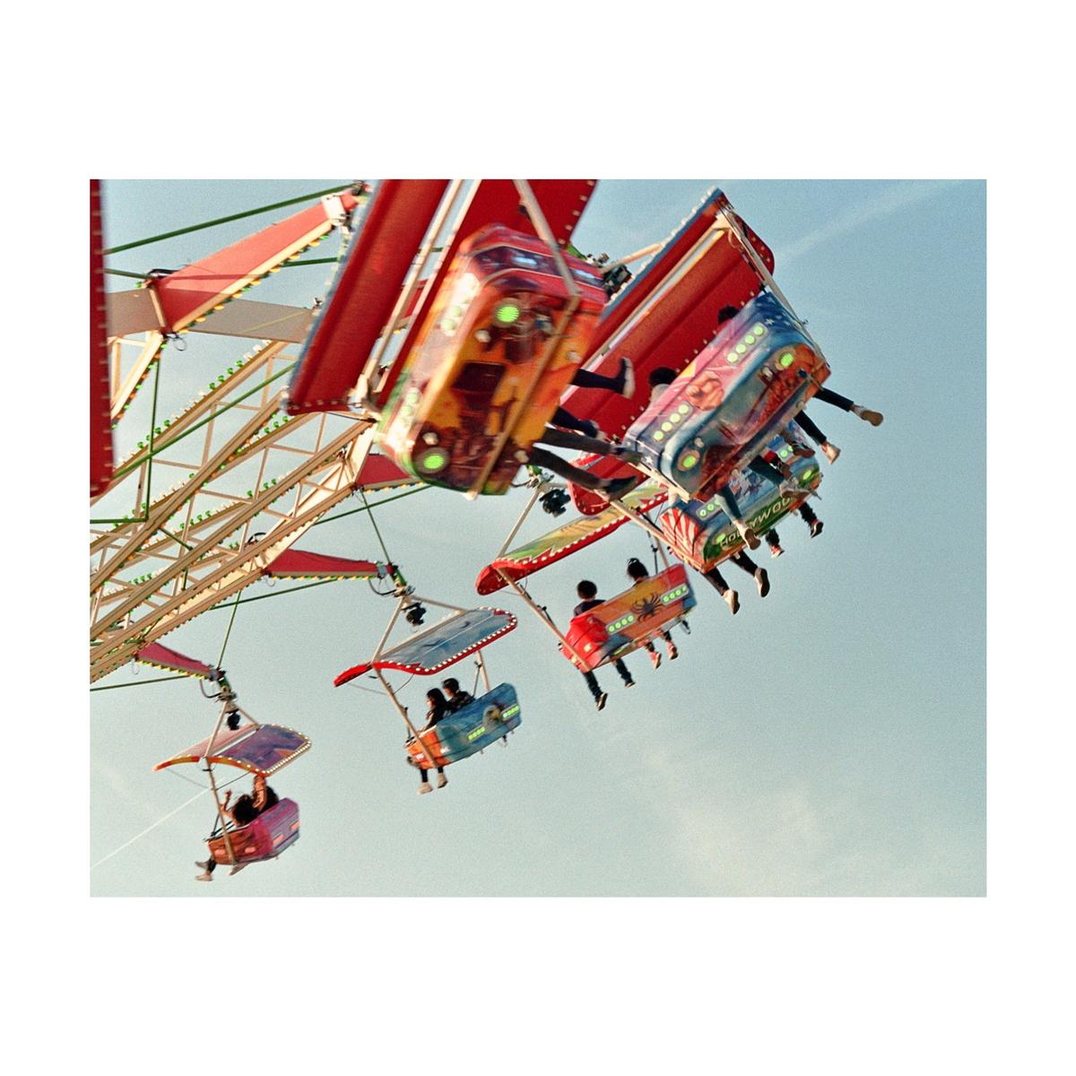 People ride a colorful swing ride at a funfair against a clear sky.