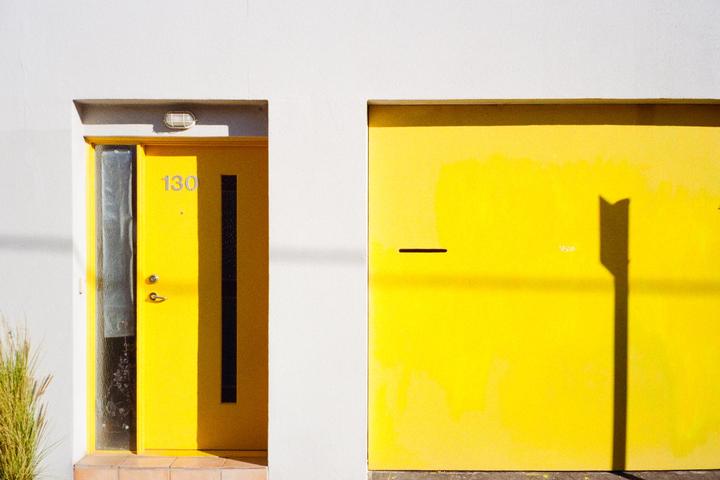 A bright yellow door with the number 130 and a yellow garage door are set into a white wall.