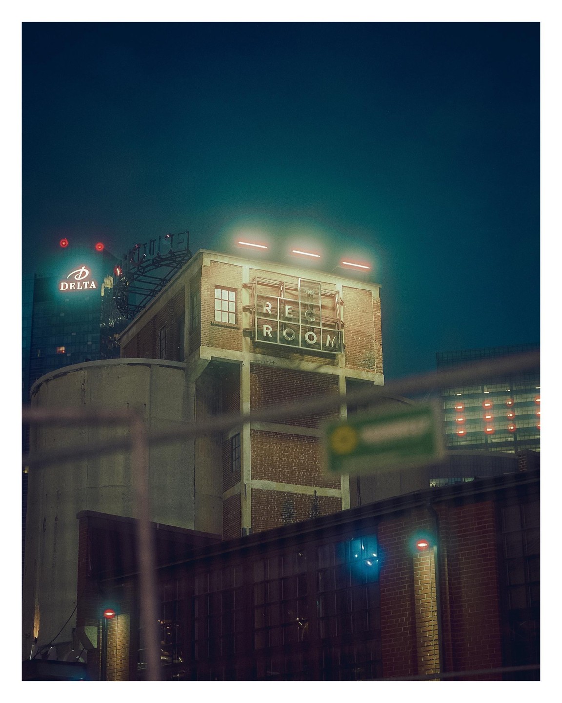 A brick building with a "Rec Room" sign is illuminated by neon lights at night.