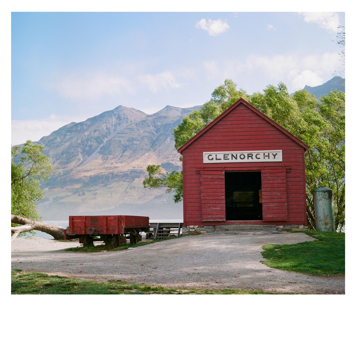 A red shed with "GLENORCHY" written on it stands near a body of water with mountains in the background.