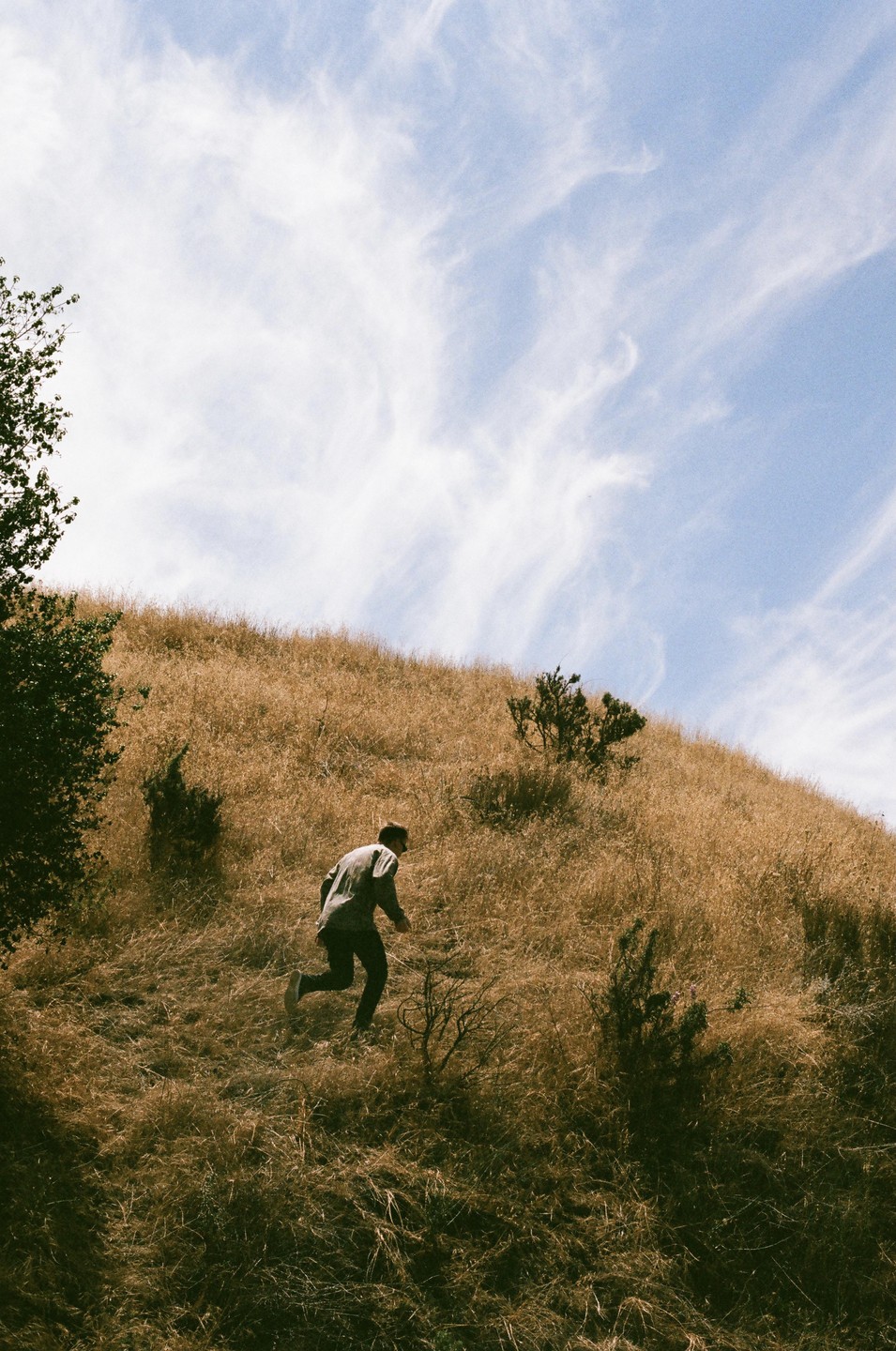 A man runs up a dry grassy hill under a blue sky with wispy clouds.