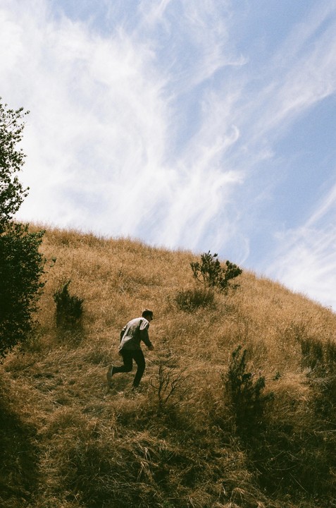A man runs up a dry grassy hill under a blue sky with wispy clouds.