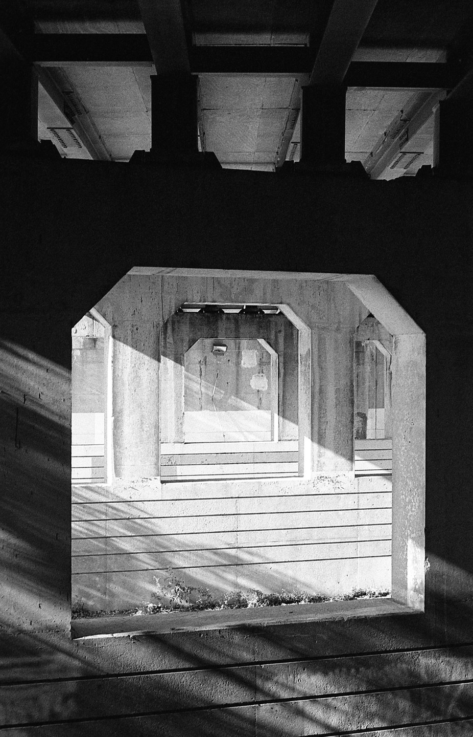 Sunlight casts shadows on the concrete walls of an underpass, creating a repeating pattern of geometric shapes.