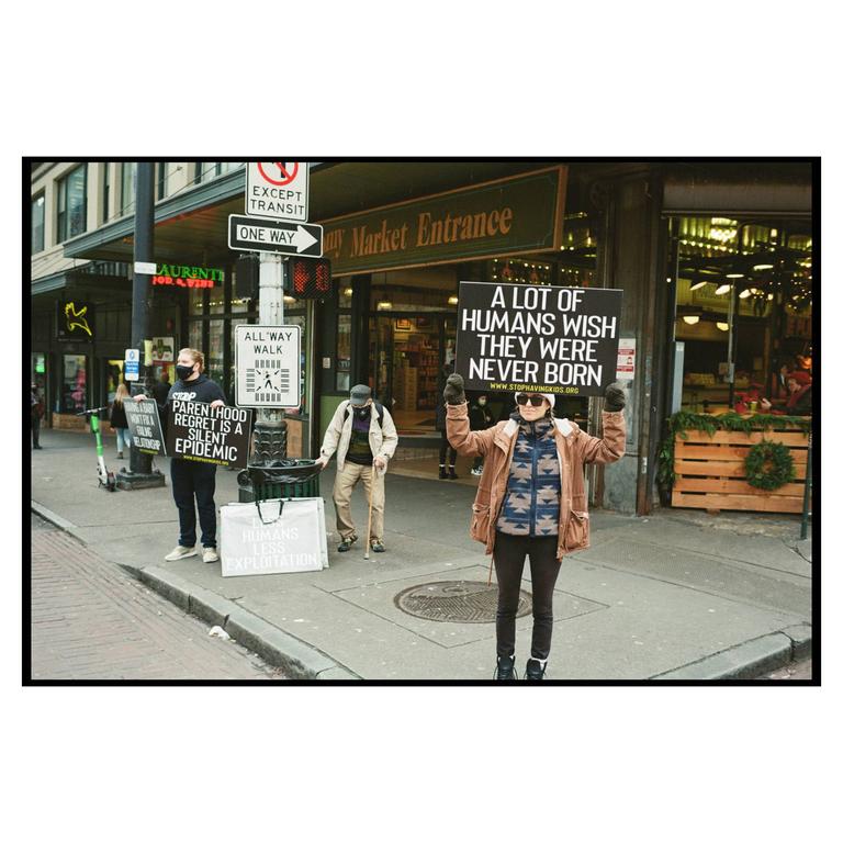 A woman holds a sign that reads "A lot of humans wish they were never born" on a city street.