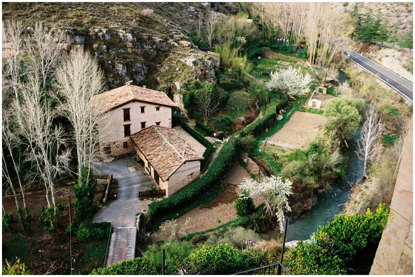 Two houses with tiled roofs sit in a valley next to a river and a road.