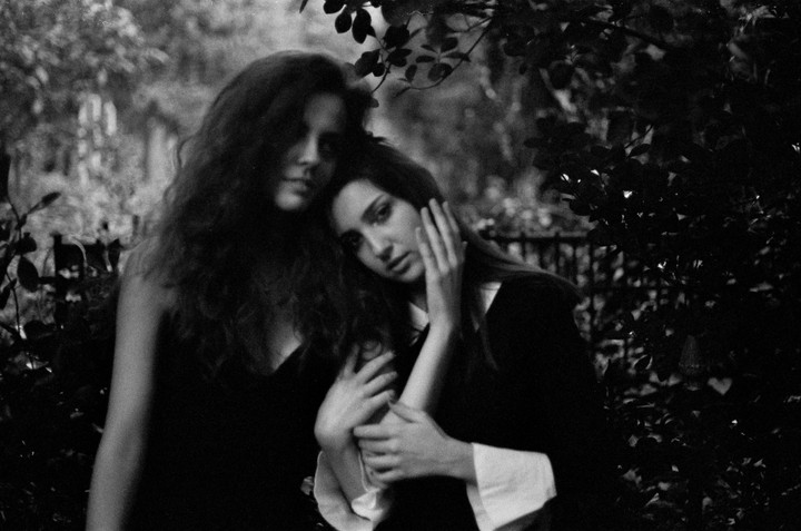Two women with long hair embrace each other in a garden.