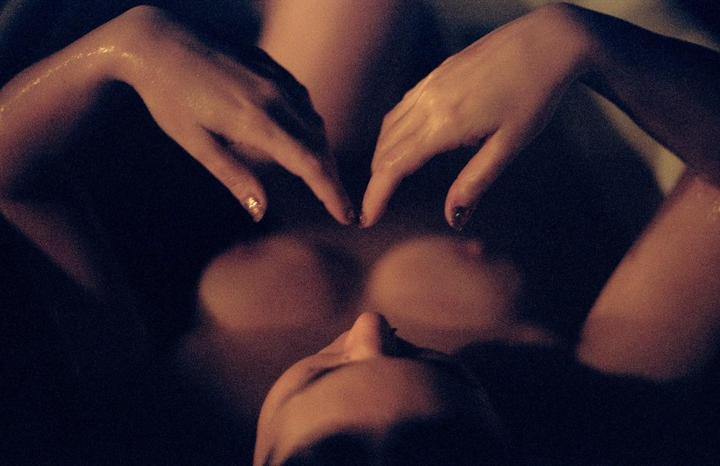 A woman lies in a bath with her hands forming a heart shape over her chest.