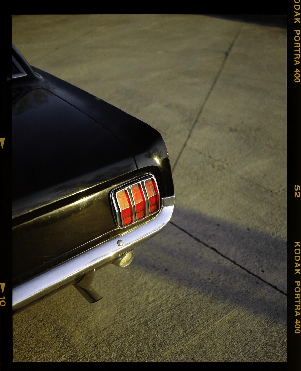 The rear of a black car with red taillights and a chrome bumper is parked on asphalt.