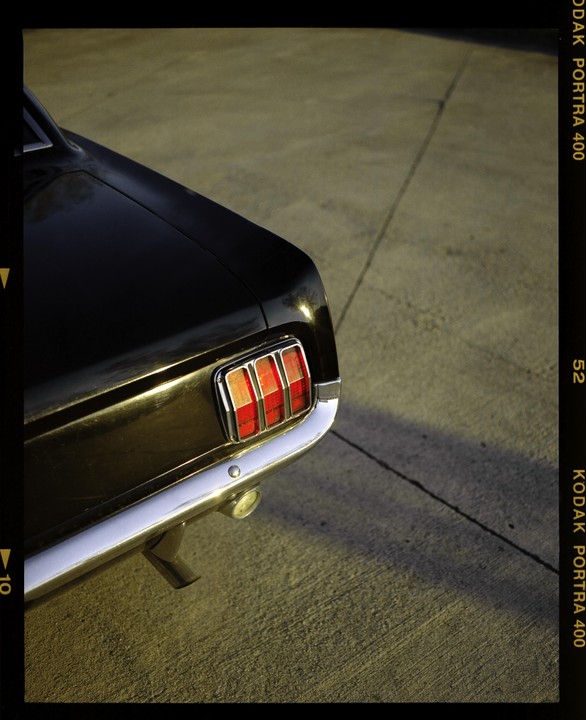 The rear of a black car with red taillights and a chrome bumper is parked on asphalt.