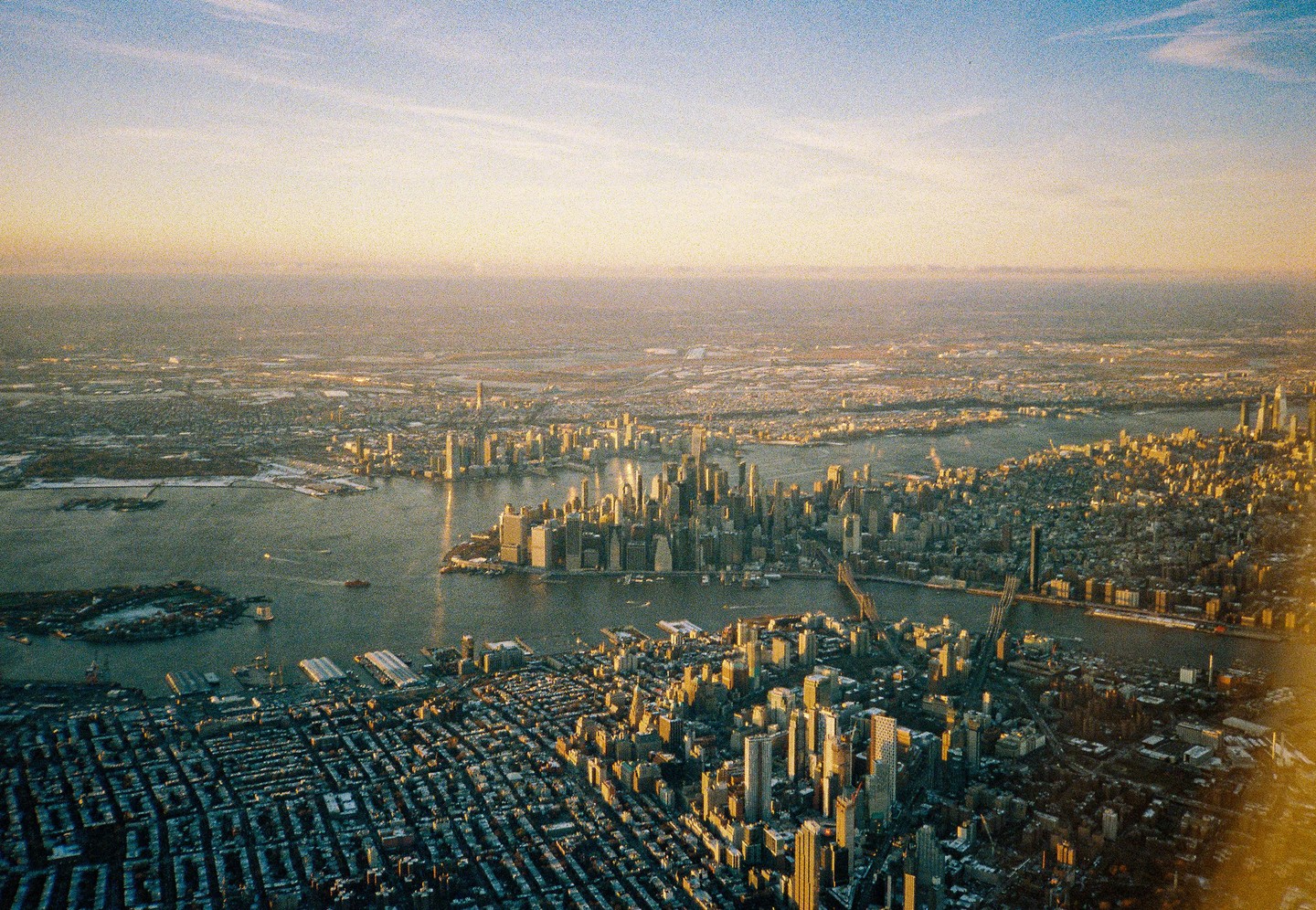 An aerial view shows the New York City skyline and surrounding areas during golden hour.