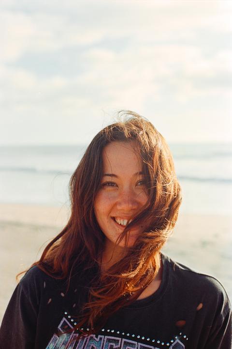 A woman with long hair smiles at the camera on a beach.