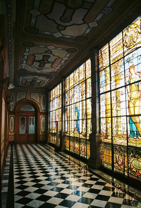 A long hallway with a checkered floor and a wall of stained glass windows is visible.