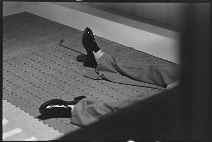 A person's legs and feet in dress shoes are visible on a patterned rug.