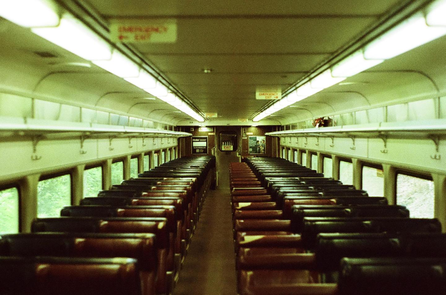 An empty train car with rows of seats on either side of an aisle is illuminated by overhead lights.