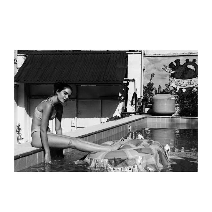 A woman sits on the edge of a swimming pool with her feet in the water, next to an inflatable ring.